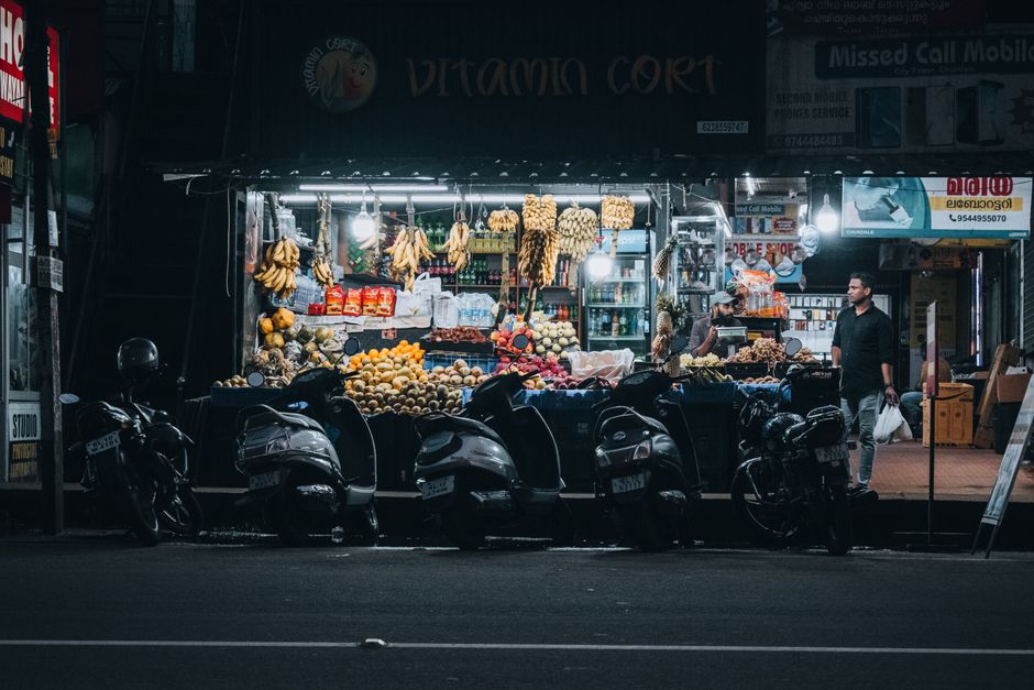 Evening view of a bustling market stall in Wayanad, India, with motor scooters parked nearby.