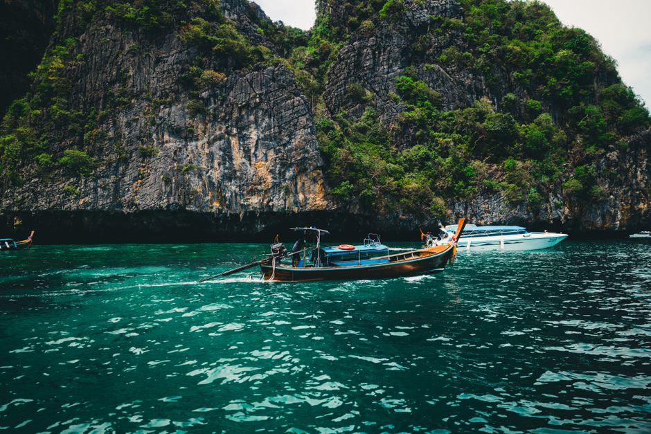 Longtail boat gliding on emerald waters against rocky cliffs in Phuket, Thailand.