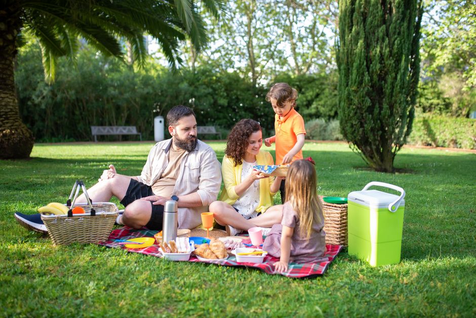 A family having a joyful picnic in a sunny park with fresh food and drinks.