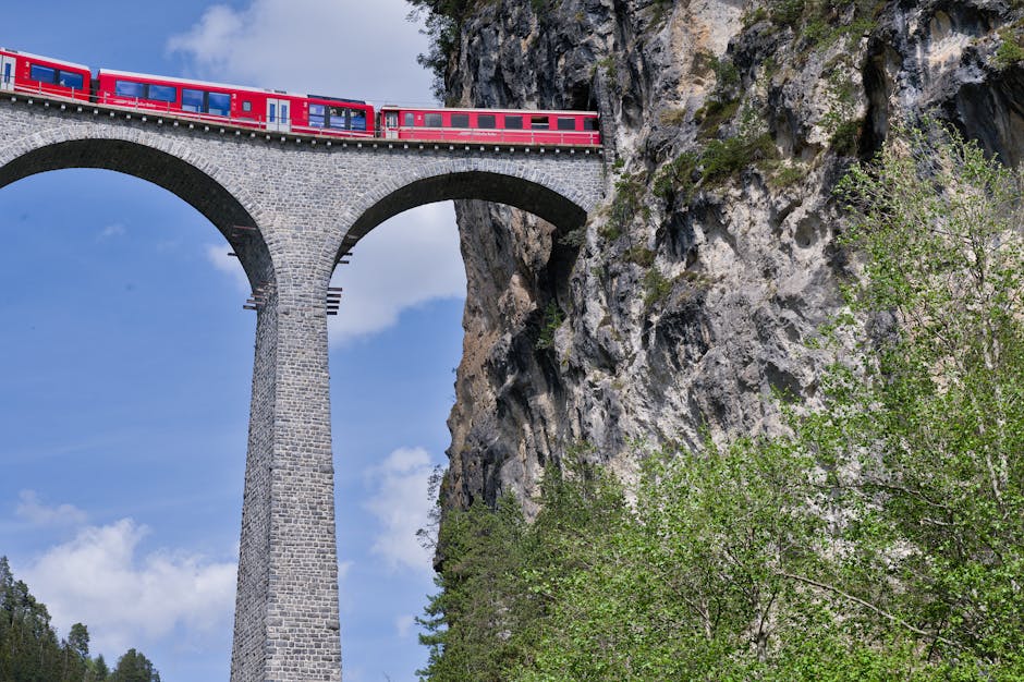 Stunning view of a red train crossing the Landwasser Viaduct in the Swiss Alps, framed by rocky cliffs.