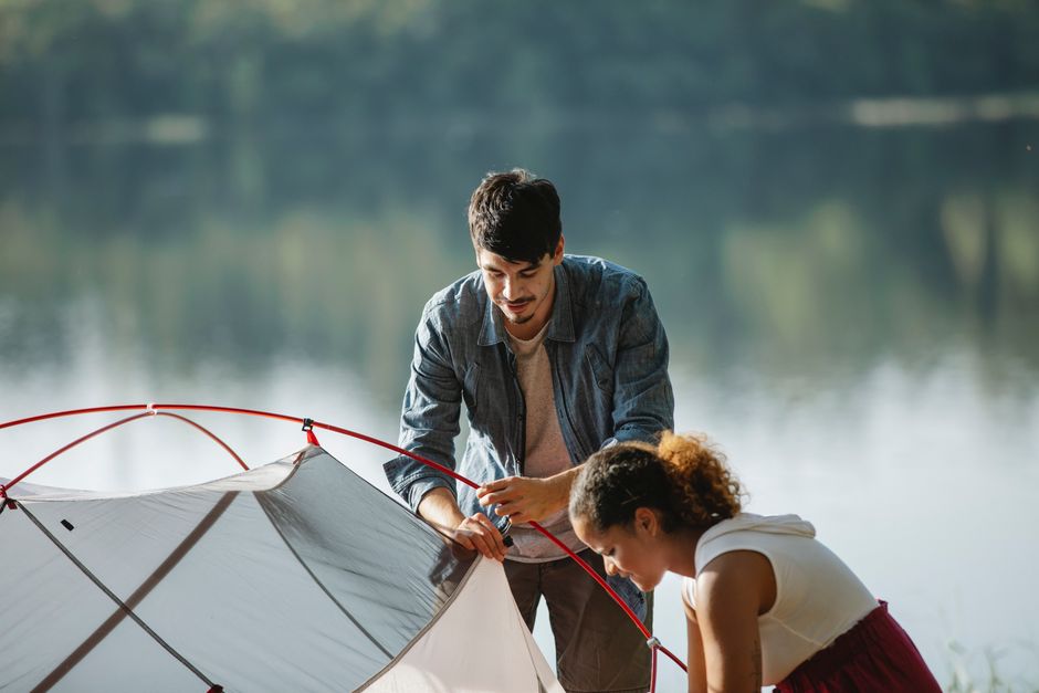 Concentrated young multiracial couple of travelers in casual wear busy with putting up near river