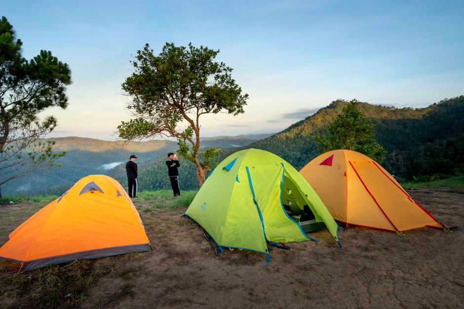 Anonymous travelers admiring view of picturesque mountain valley while spending time in camp near tents