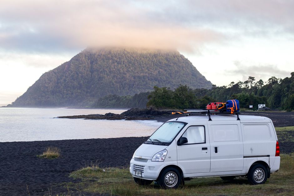 A white van parked by a foggy volcano in Chaitén, Chile, showcasing adventure and nature.