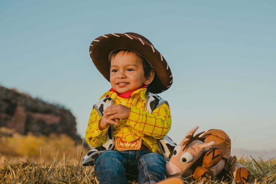 Adorable child in cowboy costume sitting outdoors with a toy. Bright, joyful atmosphere.