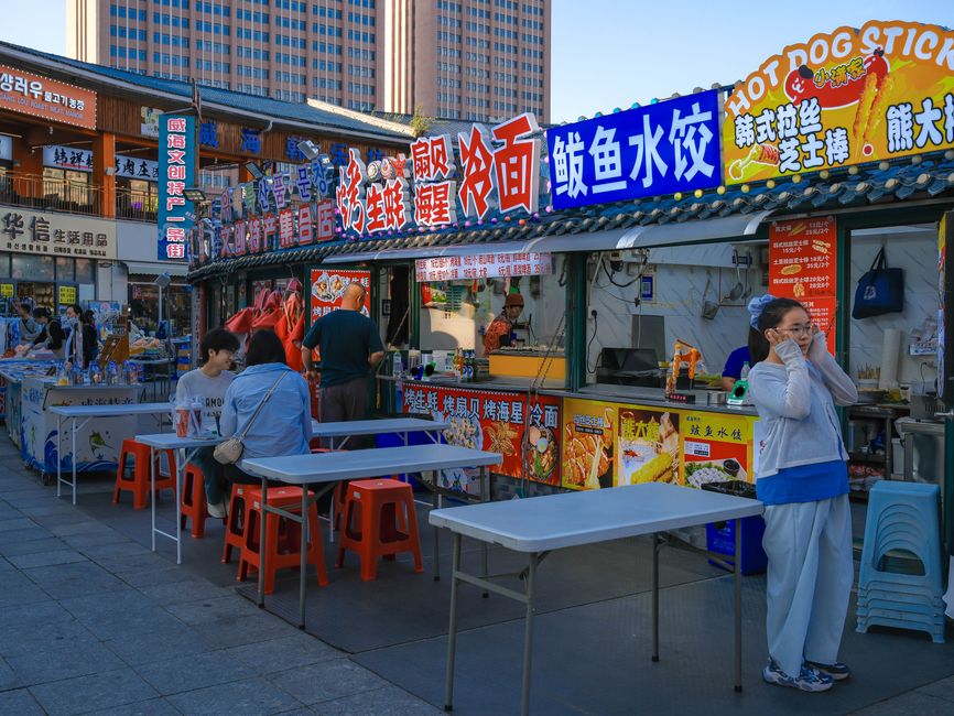 An Asian street food market bustling with people and colorful signs.
