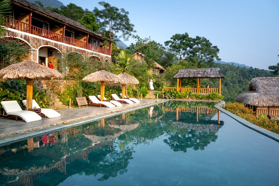 Swimming pool and sunbeds with parasols near small hotel in south eastern style in tropical resort