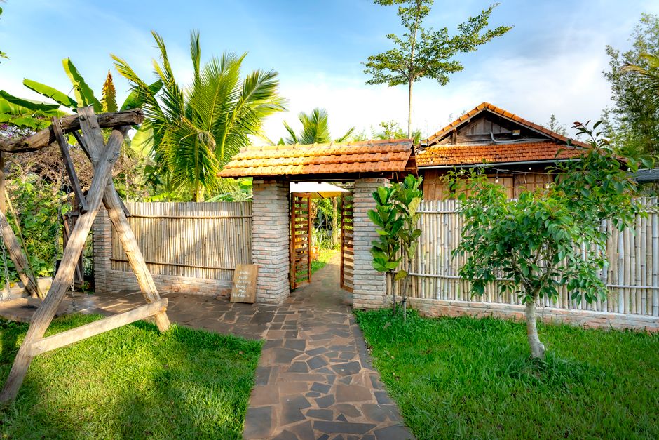 Inviting garden entrance featuring a wooden swing and lush greenery under a clear blue sky.