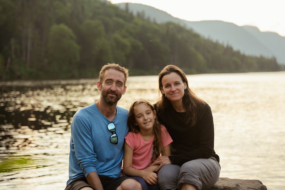 A happy family of three enjoying a serene moment beside a lake surrounded by mountains.