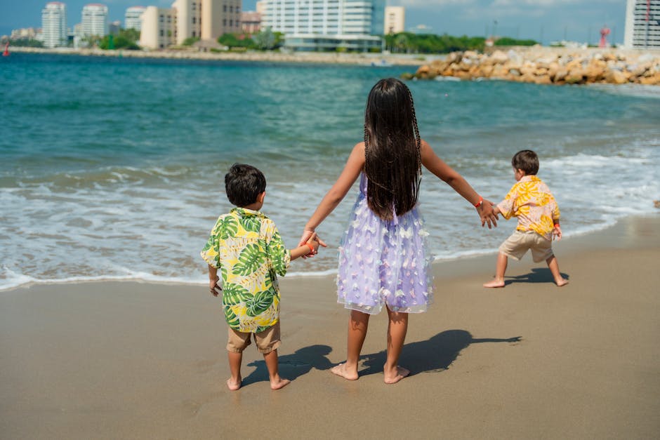Children enjoying a sunny day at the beach with waves and cityscape in the background.