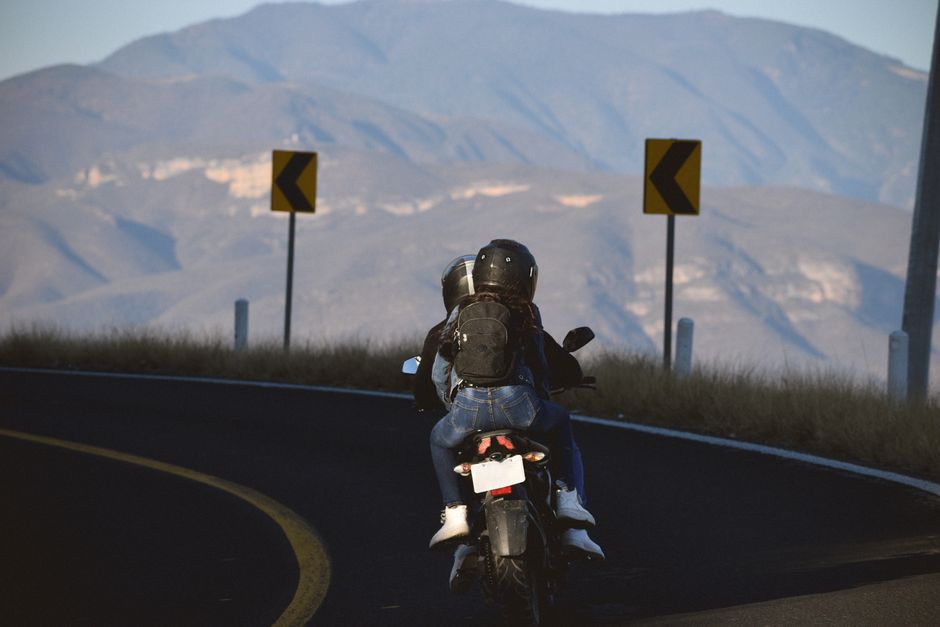 A couple on a motorcycle traveling on a winding mountain road, surrounded by scenic views.