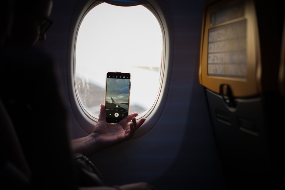 Passenger capturing a photo of the airplane wing from the cabin window during daylight flight.