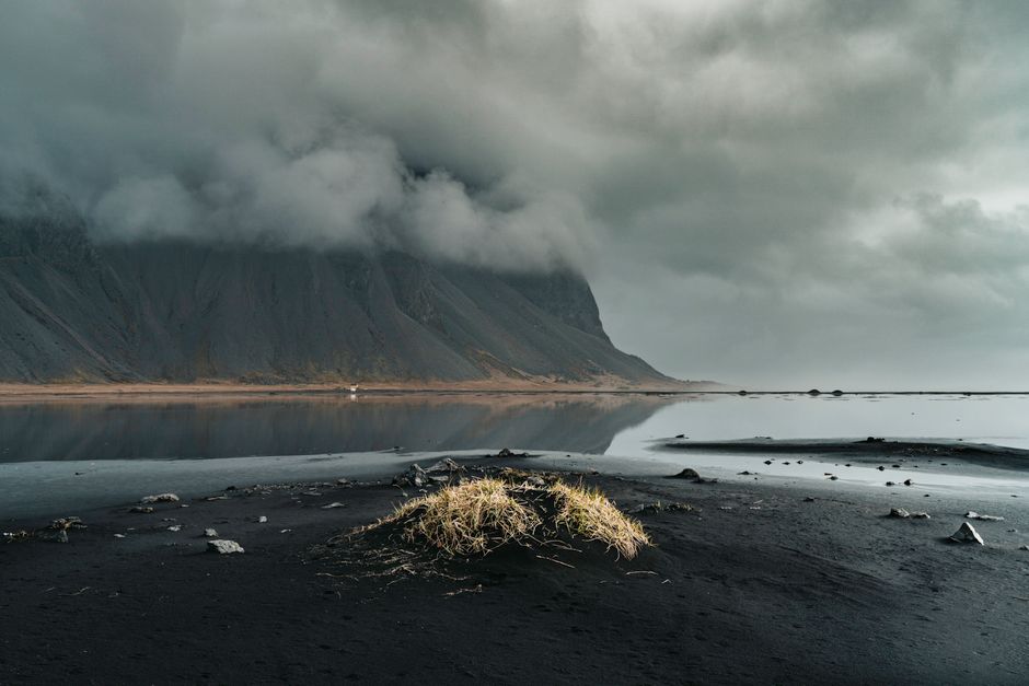 Moody Icelandic scene with mountains shrouded in clouds reflecting in a serene lake.