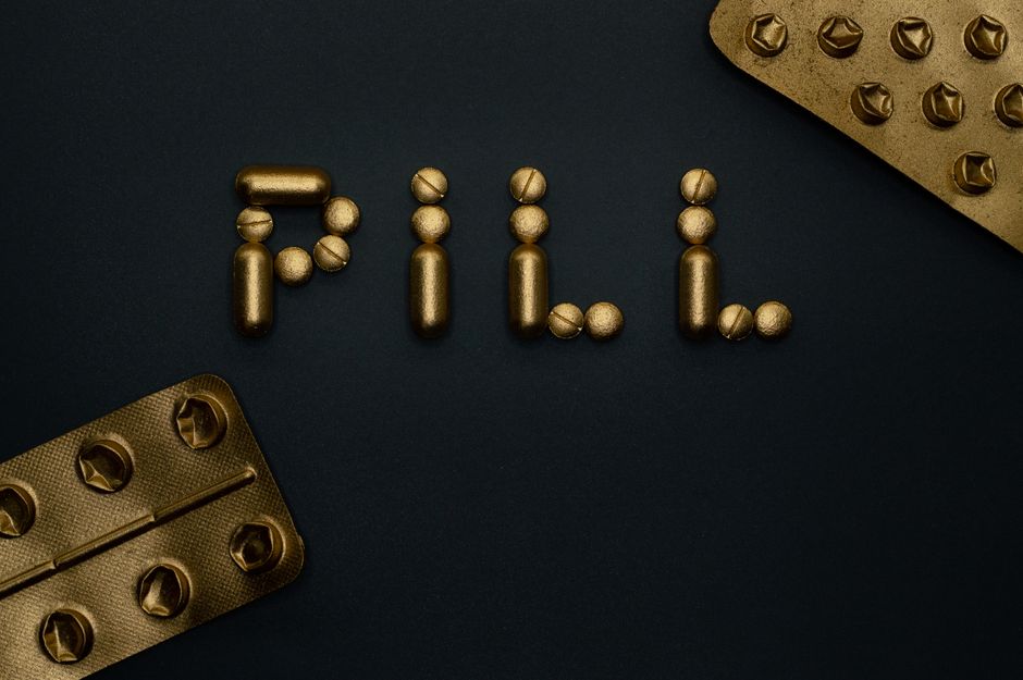 Artistic arrangement of gold pills spelling 'Pill' on a dark backdrop, emphasizing pharmaceutical concepts.