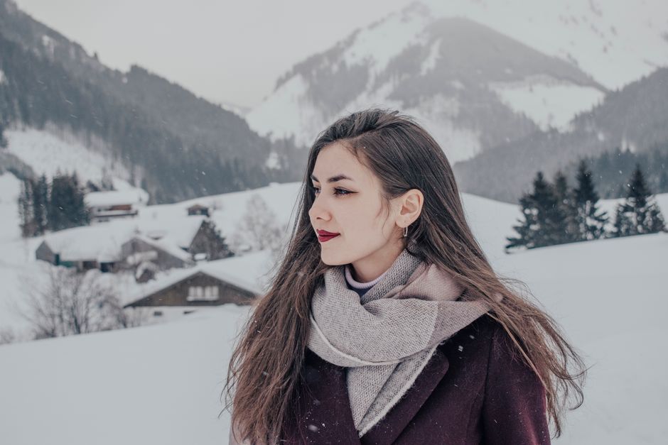 Elegant woman in winter clothing, surrounded by snowy alpine landscape with cabins.