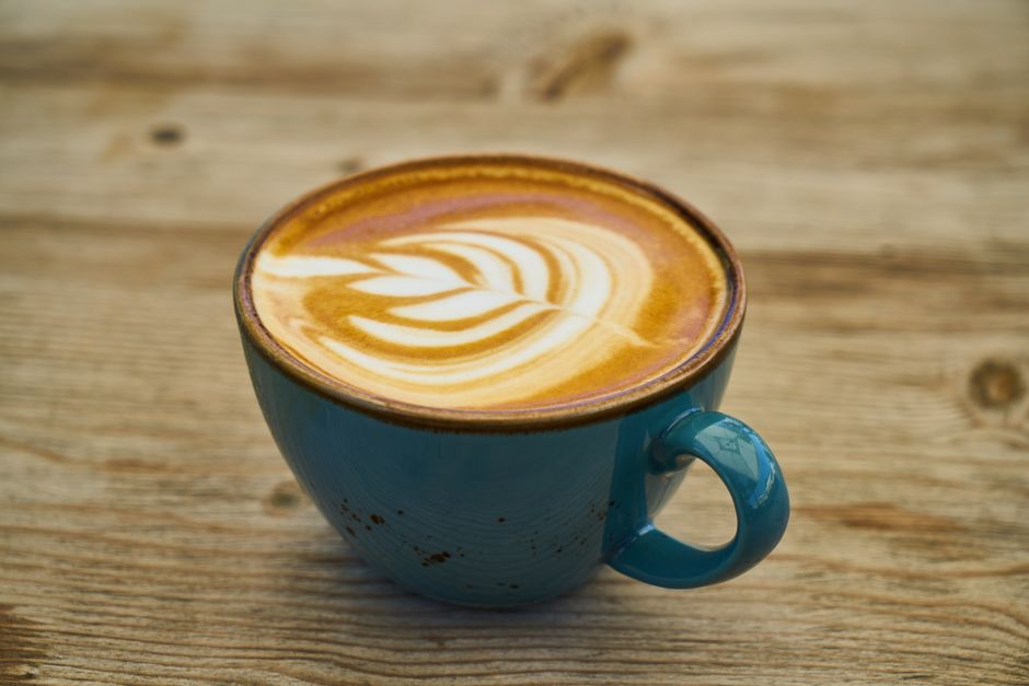 A teal ceramic mug of latte art coffee on a rustic wooden table, creating a warm and inviting scene.