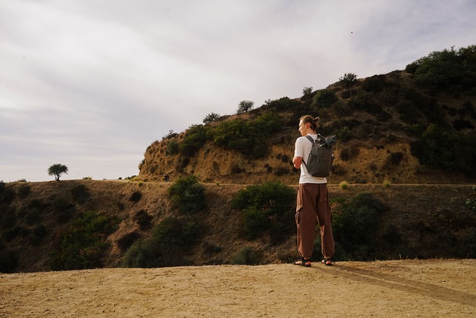 Man with backpack exploring hilltop trail under cloudy sky.