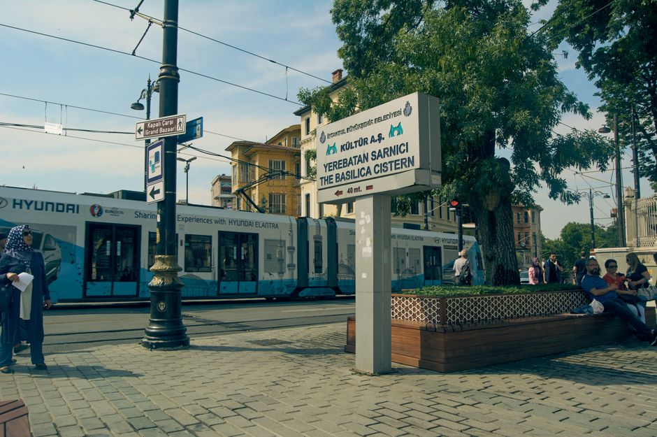 A city tram passes by the Basilica Cistern sign in Istanbul, showcasing a blend of modern and historic elements.