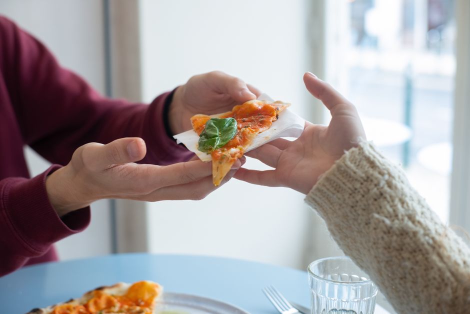 Two people enjoying and sharing a slice of delicious pizza in a cozy indoor setting.