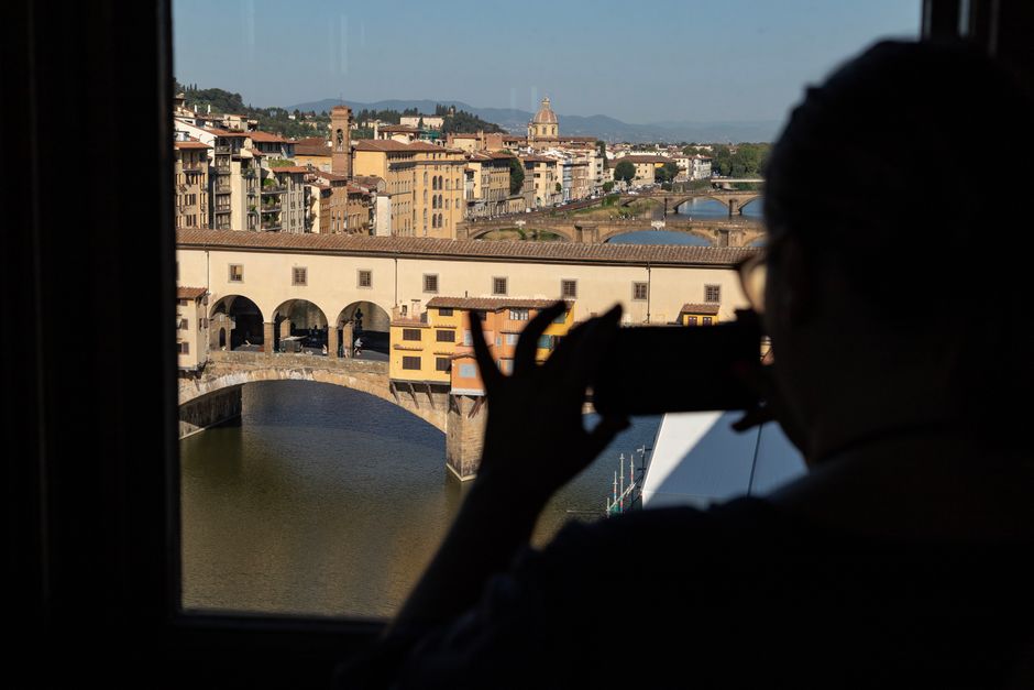 Silhouette of a person photographing Ponte Vecchio in Florence with cityscape beyond.