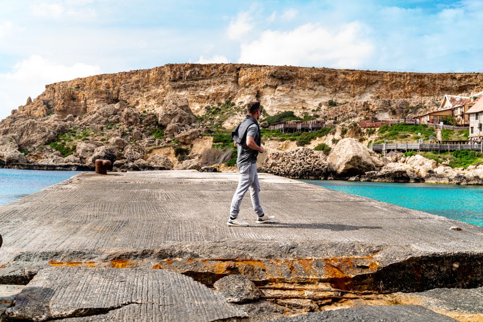 Discover the stunning coastal cliffs of Malta with a lone traveler on a vibrant sunny day.