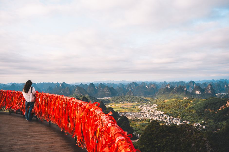 Traveler admiring stunning panorama from Fubo Hill, Guilin, with vibrant red ribbons and limestone mountains.