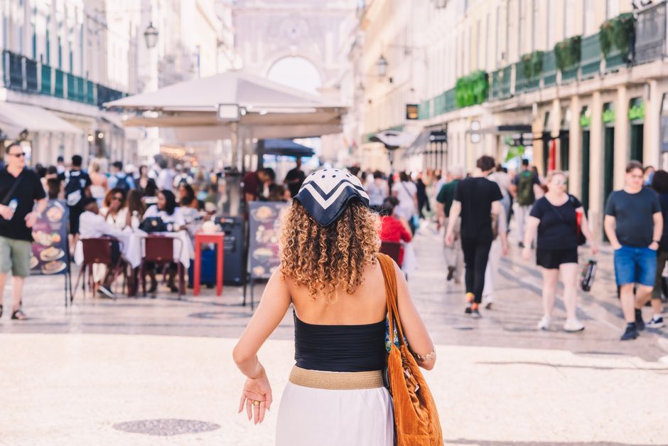A fashionable woman wanders through a bustling city street alive with activity and culture.