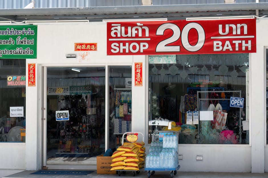 Street view of a budget shop in Thailand with bilingual signage and goods outside.