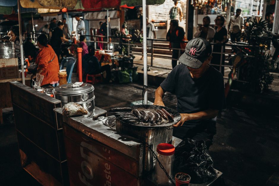 A bustling night market scene with a street vendor cooking food under colorful tents.